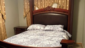 Ein Schlafzimmer mit einem hölzernen Bett, einem Nachttisch, einem dekorativen Kopfteil und Vorhängen.