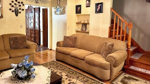 Ein Wohnzimmer mit einer Couch, einem Couchtisch mit Blumenarrangement, einer Kandelaber und einer Treppe.