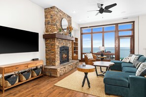 A living room with a stone fireplace, a flat-screen TV, a large window with a view, and a cozy seating area.