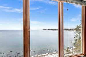 A view through a window with wooden frames, a clear sky, and a calm body of water.