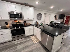 Una cocina moderna con armarios blancos, electrodomésticos de acero inoxidable, una isla con encimera negra y un tapete estampado.