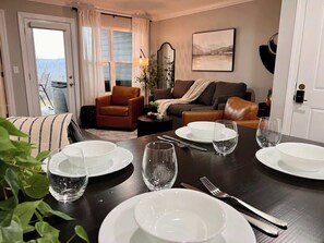 Una mesa de comedor con platos, vasos y cubiertos, un sofá, una silla y un espejo en una habitación con una puerta y una ventana.