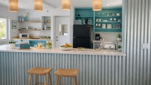 Una cocina moderna con una isla central, taburetes de bar, un refrigerador negro, armarios color aguamarina y lámparas colgantes de mimbre.