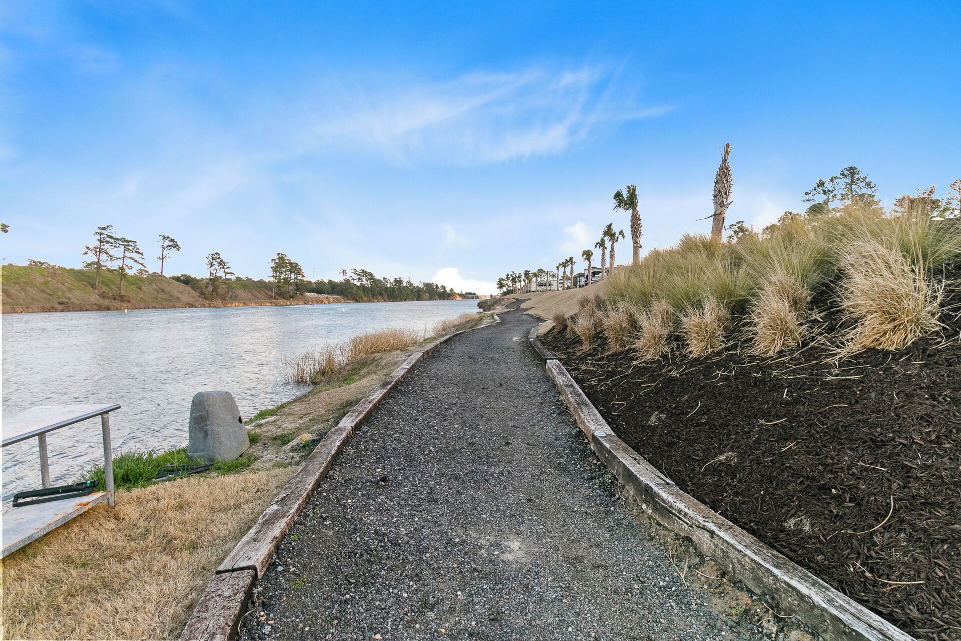 A gravel path alongside a body of water, bordered by grass and trees.