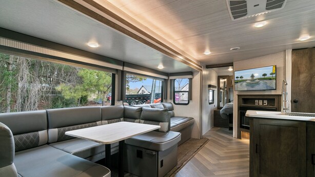 Ein modernes Wohnmobil-Interieur mit Essbereich, Sitzgelegenheiten, einer kleinen Küche und großen Fenstern mit Aussicht.