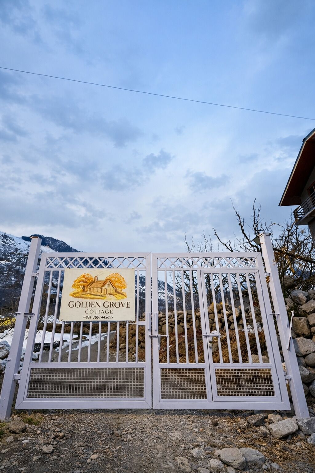 Une entrée fermée par un portail, avec une pancarte indiquant « Golden Grove Cottage », et une chaîne de montagnes en arrière-plan.