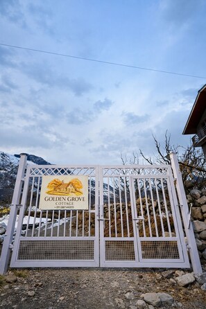 Una entrada cerrada con un letrero que dice 'Golden Grove Cottage' y montañas al fondo.