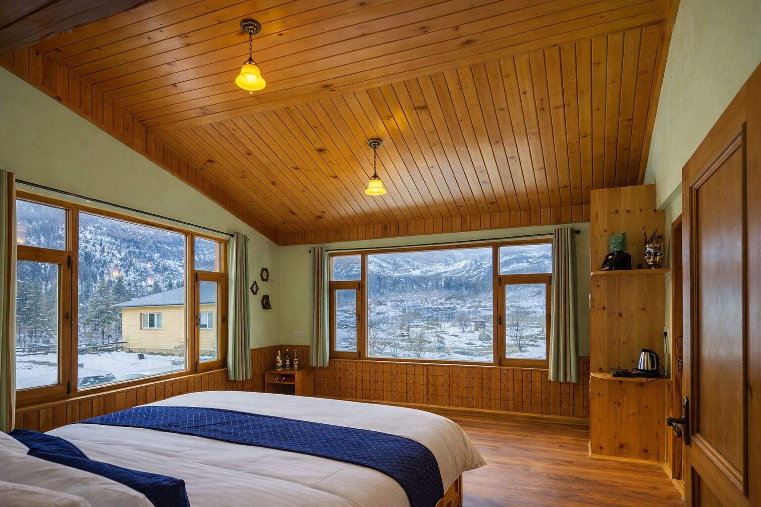 A bedroom with a large bed, wooden ceiling, and windows with a snowy landscape view.