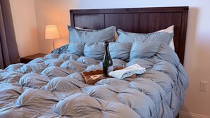 A neatly made bed with a blue duvet, a bottle, and a glass on the bed. - Furnished 3BR/3BA Brand New Anaheim Condo Move-In Ready & Utilities Included (Anaheim)