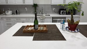 A kitchen with white cabinets, a countertop, a bottle of champagne, a glass, a water bottle, and a potted plant. - Furnished 3BR/3BA Brand New Anaheim Condo Move-In Ready & Utilities Included (Anaheim)