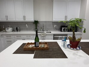Eine Küche mit weißen Schränken, einer Arbeitsplatte, einer Champagnerflasche, einem Glas, einer Wasserflasche und einem Blumentopf.