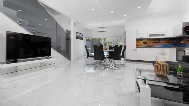 Una sala de estar moderna con televisor de pantalla plana, una mesa de centro de vidrio y un comedor con sillas.