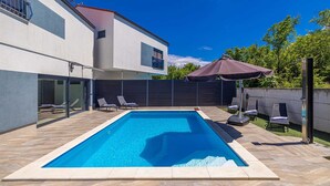 Una casa moderna con piscina, mobiliario exterior y cielo azul despejado.