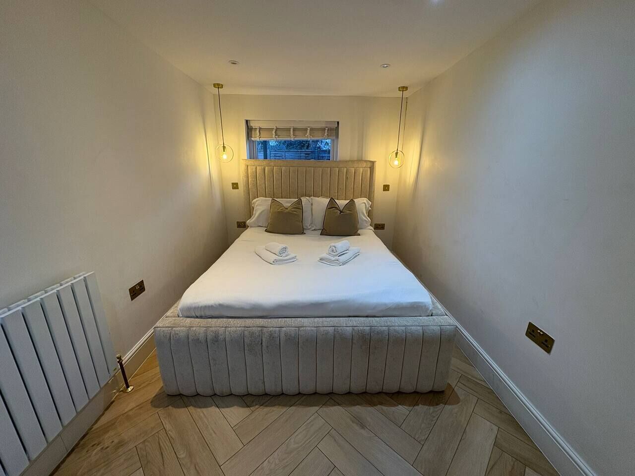 Een slaapkamer met een bed, bedlampen, een raam en een radiator.