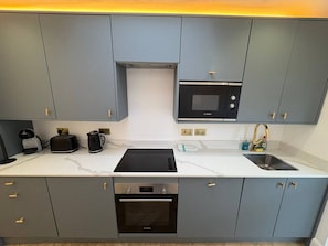 Eine moderne Küche mit grauen Schränken, einer Bosch-Mikrowelle, einem schwarzen Induktionskochfeld, einem eingebauten Backofen und einer Spüle aus Edelstahl.