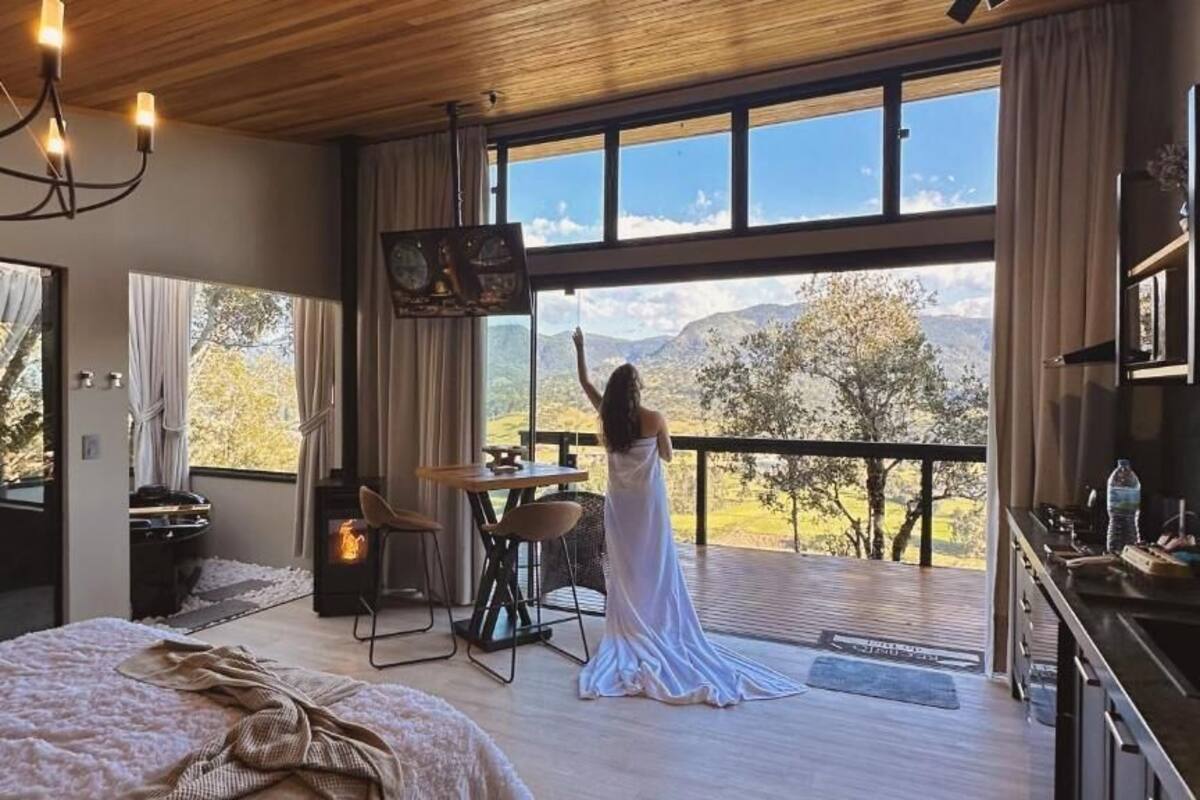 A bedroom with a large bed, a wooden ceiling, a TV, and a balcony with a view of the mountains.