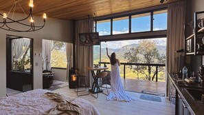 Un dormitorio con una cama grande, techo de madera, televisor y balcón con vista a las montañas.