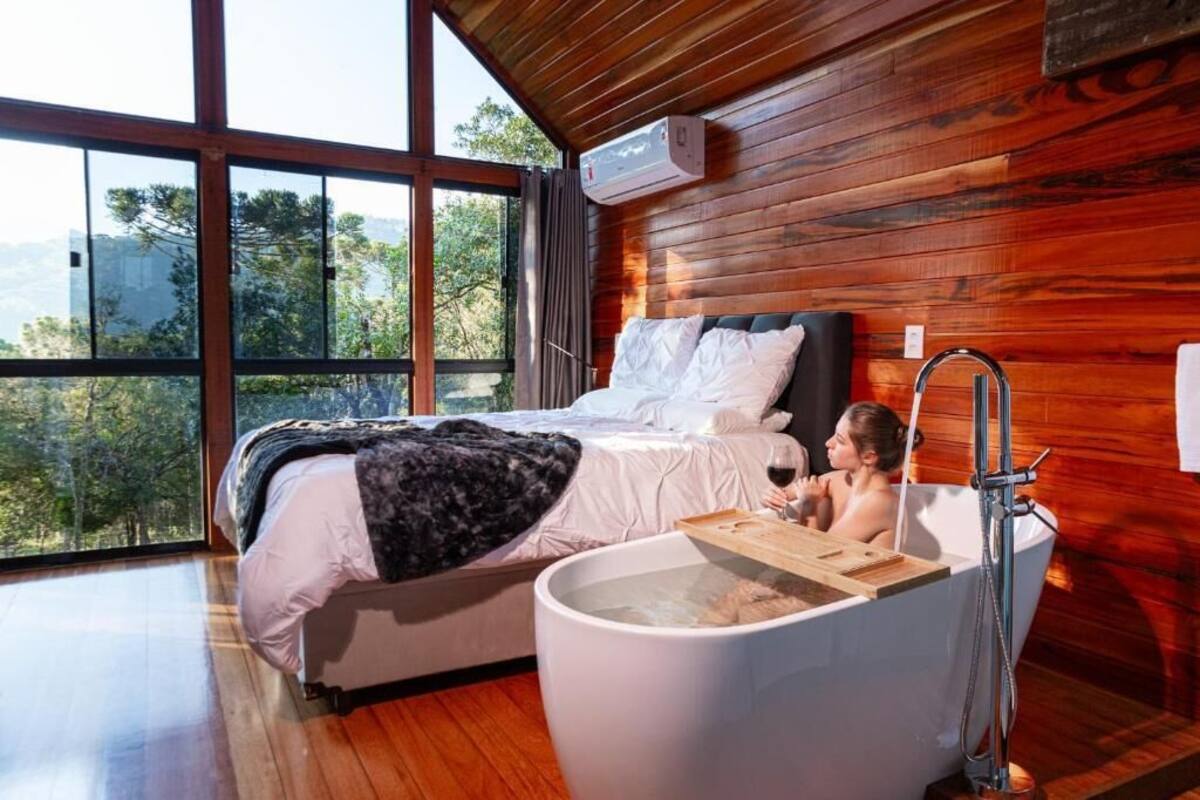 A bedroom with a large bed, a bathtub, and a window with a view of trees.