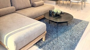 Una sala de estar moderna con un sofá, un comedor con sillas, una cocina al fondo y un ventanal grande.