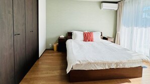 Un dormitorio con cama, mesitas de noche, armario y ventana con cortinas.