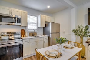 A modern kitchen with stainless steel appliances, white cabinetry, and a dining area with a marble table. - Gateway to Downtown Tacoma! Sleek Couple's Condo (Tacoma)