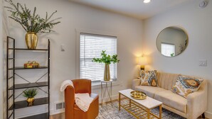 A living room with a sofa, a coffee table, a chair, a bookshelf, a window with blinds, a mirror, and a plant. - Gateway to Downtown Tacoma! Sleek Couple's Condo (Tacoma)