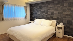 Un dormitorio moderno con una cama grande, una mesita de noche, aire acondicionado de pared y una ventana con cortinas traslúcidas.
