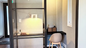 Una habitación con un divisor de vidrio corredero, un escritorio con silla, un armario pequeño y un cuadro colgado en la pared.