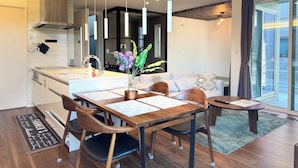 Una cocina moderna con una isla central, iluminación colgante y una zona de comedor con mesa y sillas de madera.