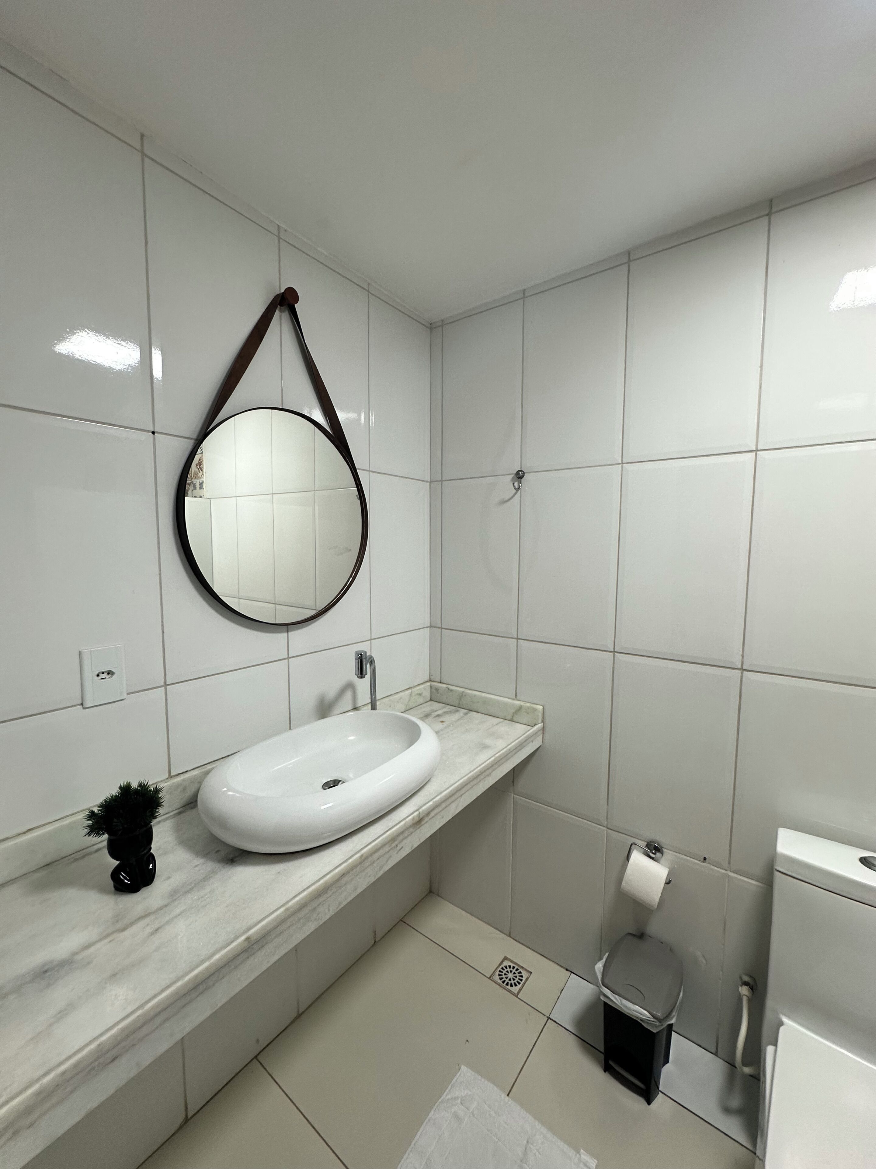 Une salle de bain avec un lavabo blanc, un miroir rond et des toilettes.
