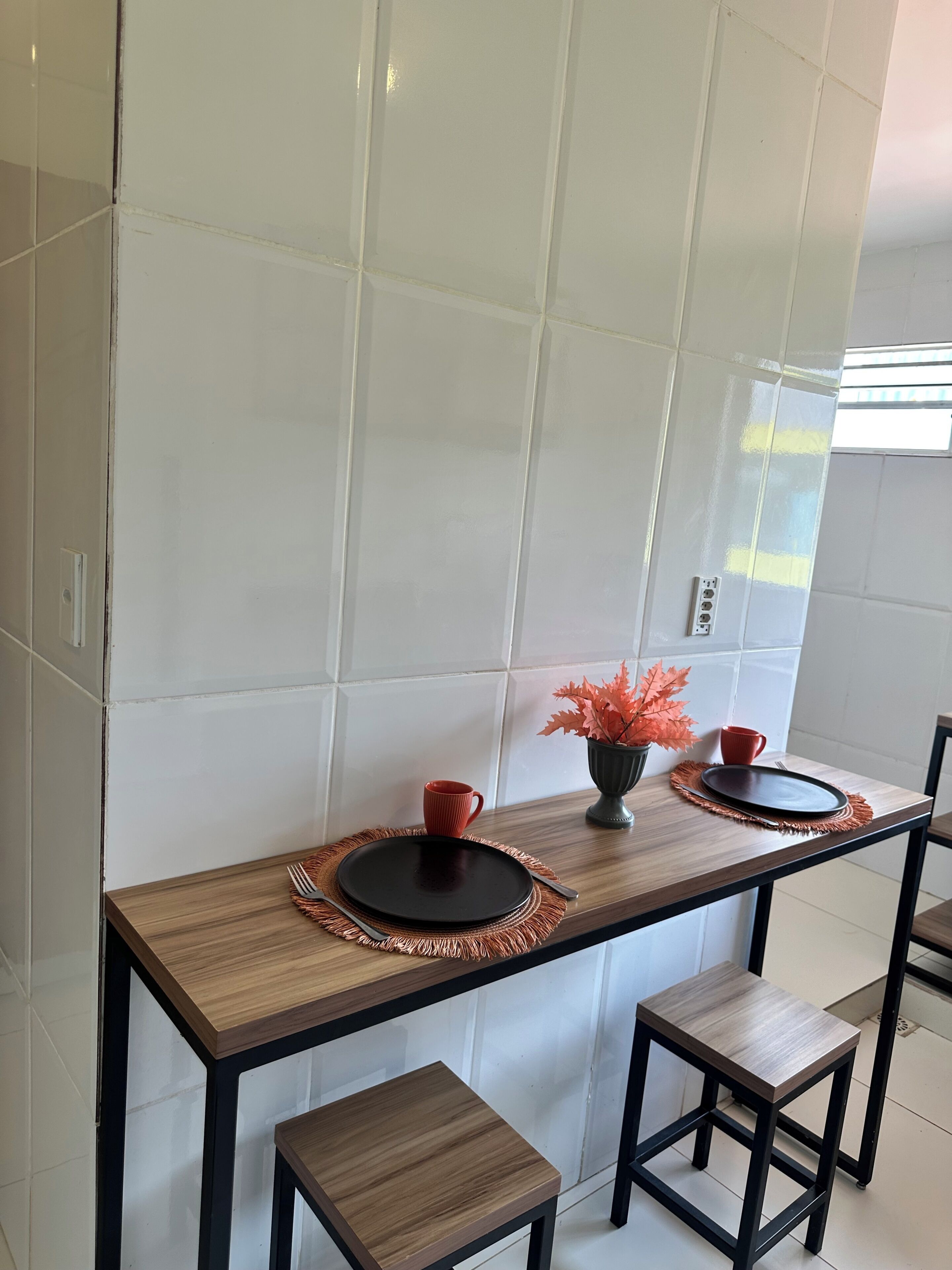 A modern kitchen with a wooden countertop, two stools, and a decorative vase with orange leaves.