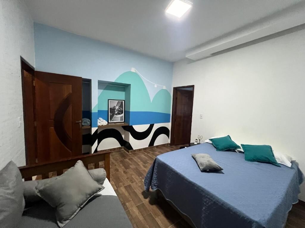 Quarto com uma cama, uma cadeira, um guarda-roupa de madeira e uma parede com um design abstrato azul e branco.