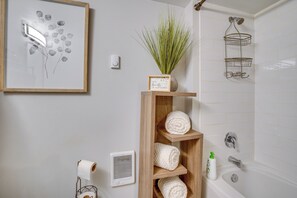 A bathroom with a shower, a wooden shelf with towels, a framed picture, and a potted plant. - Work & Explore Downtown Tacoma! Convenient Condo (Tacoma)