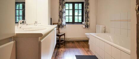 A bathroom with a wooden floor, a bathtub, a toilet, a sink, and a window with curtains.