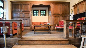 Una habitación tradicional con paneles de madera, un banco y sillones tapizados en rojo.