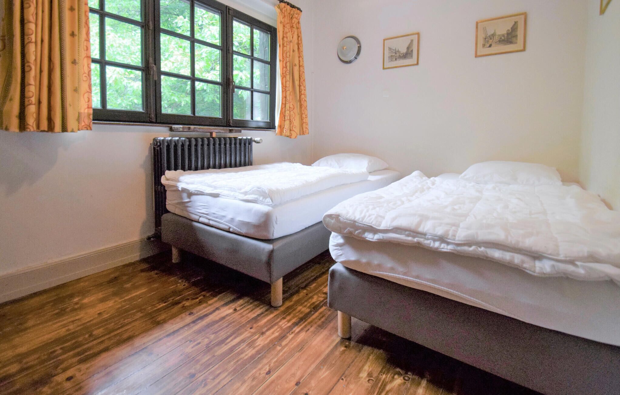 A room with two single beds, a radiator, a window with curtains, and a wall clock.