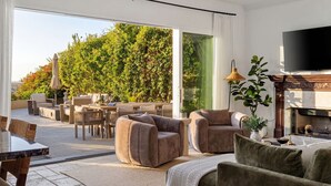 A modern living room with a fireplace, a flat-screen TV, and a large sliding glass door leading to an outdoor patio. - Luxury Pacific Beach Hilltop Rooftop Deck, Pool, 14-Person Hot Tub, 6BR/5BA (San Diego)