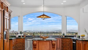 A spacious kitchen with a large island, wooden cabinets, and a view of a cityscape through an arched window. - Luxury Pacific Beach Hilltop Rooftop Deck, Pool, 14-Person Hot Tub, 6BR/5BA (San Diego)