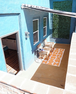 Ein blaues Gebäude mit einer Terrasse, die einen gemusterten Teppich, Holzstühle und einen Tisch zeigt.