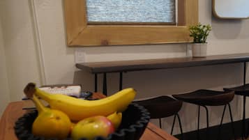 A wooden table with a black bowl containing fruits, a potted plant, and a window with a view.