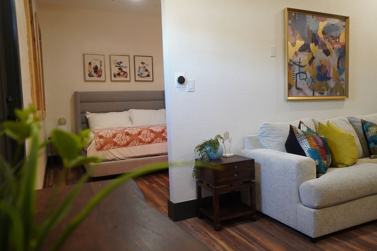 Una habitación con una cama, un sofá, una mesita con una planta y un cuadro en la pared.