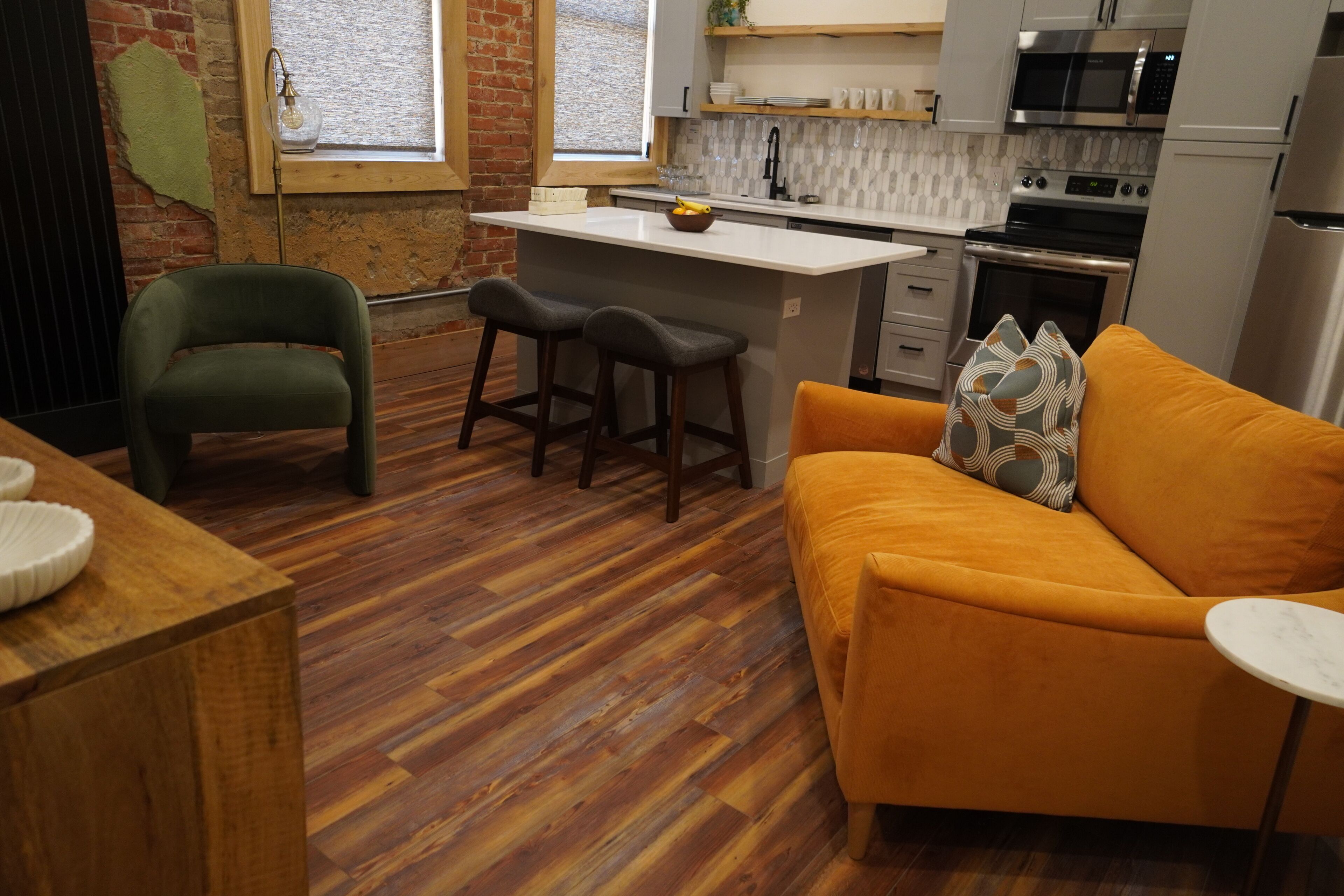Una cocina con una isla central, taburetes de bar, un sofá y una mesa de comedor de madera.