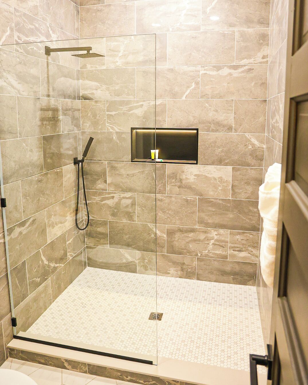 Een douche met een glazen deur, een handdouche en een bedieningspaneel aan de muur.