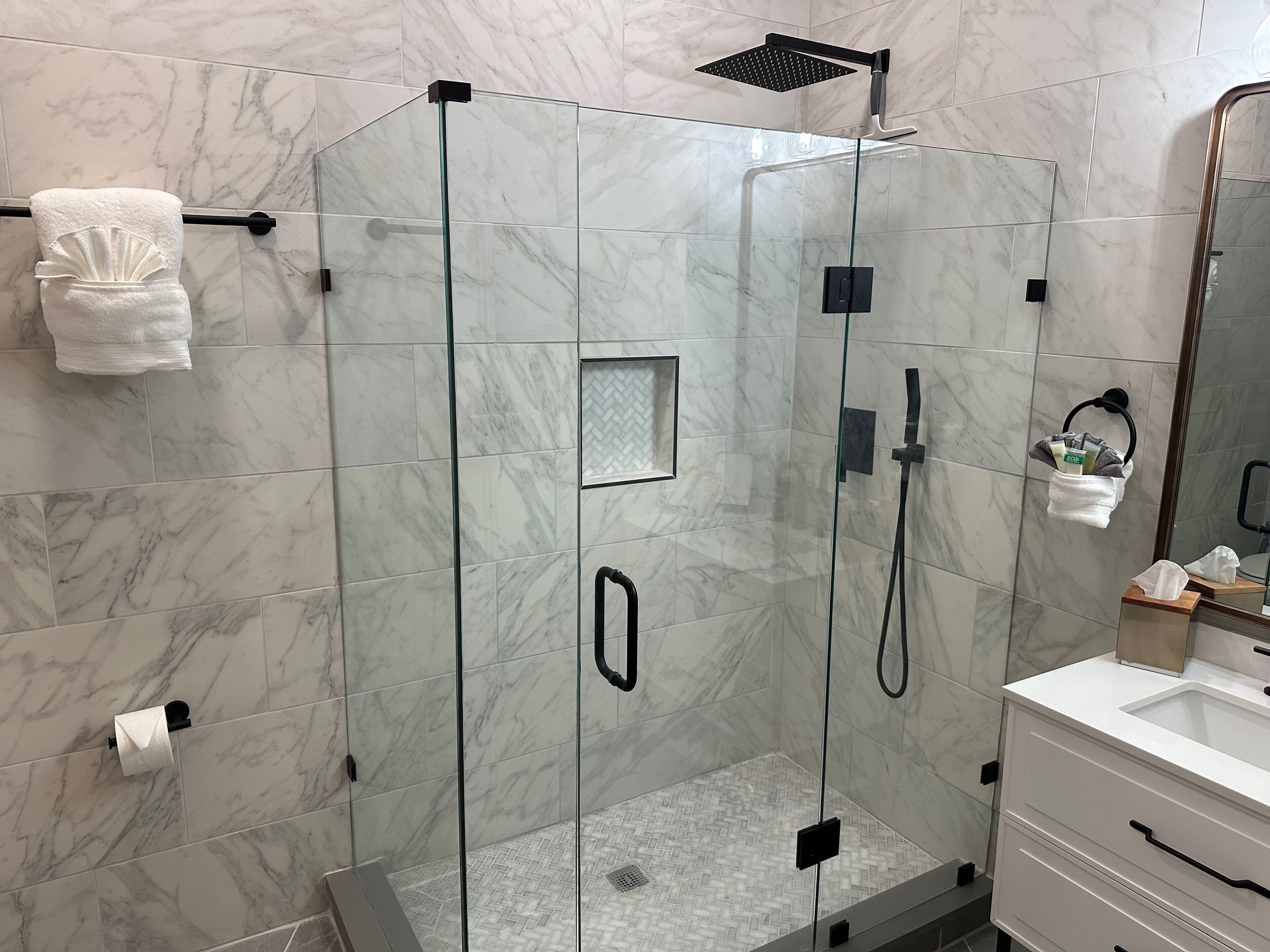 A modern bathroom with a glass-enclosed shower, marble tiles, a towel rack, and a mirror.