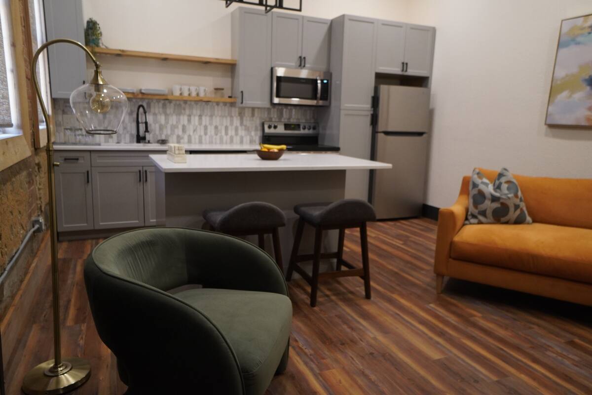 Una cocina moderna con armarios grises, encimera blanca y una isla central con taburetes.