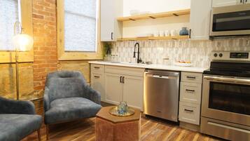 A modern kitchen with white cabinets, a stainless steel dishwasher, and an oven. There is a wooden coffee table with a glass vase.