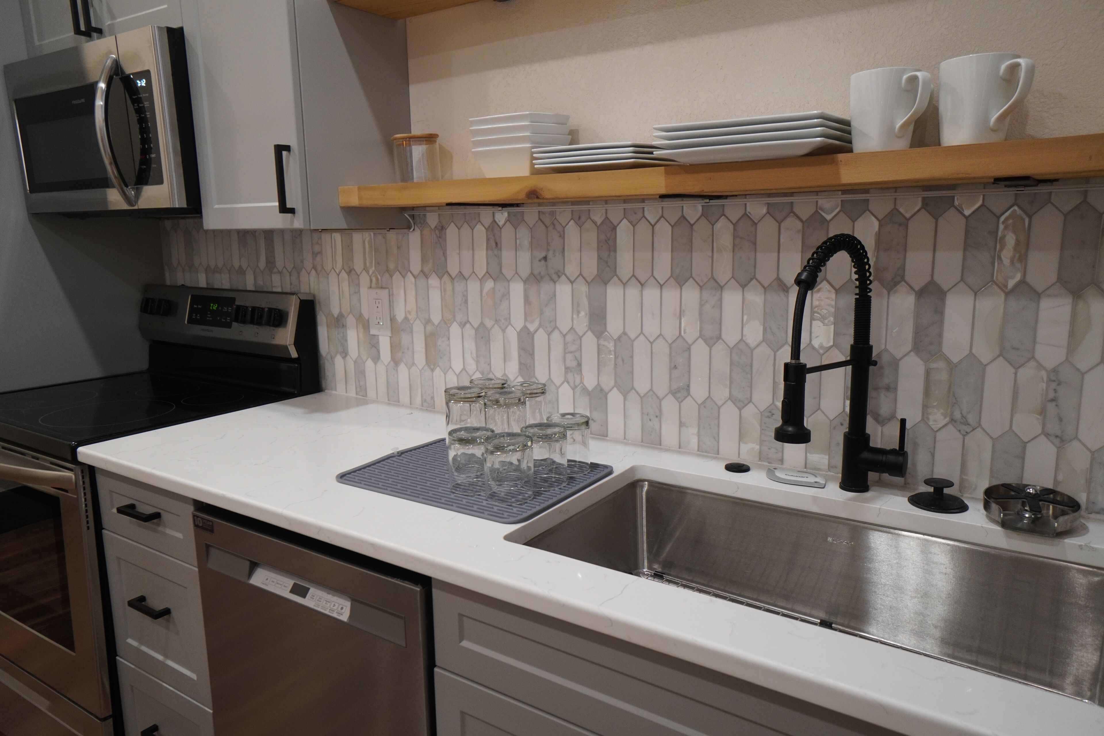 A modern kitchen with a stainless steel sink, a microwave, a stove, and a tiled backsplash.
