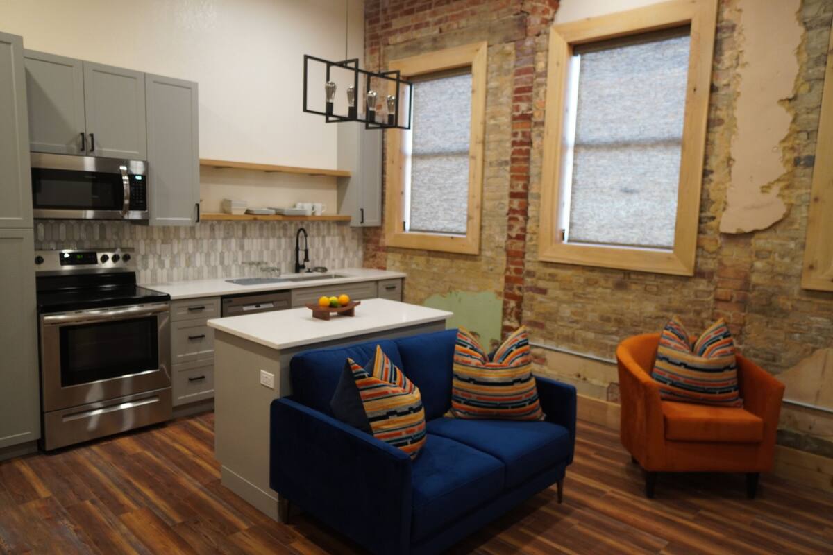 Una cocina moderna con electrodomésticos de acero inoxidable, un sofá azul y un sillón naranja.
