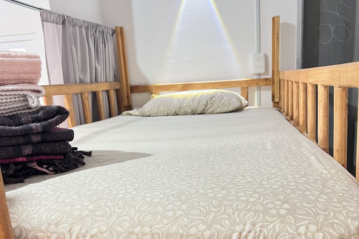 A single bed with a floral-patterned bedspread, wooden headboard, and a stack of folded blankets on the left.