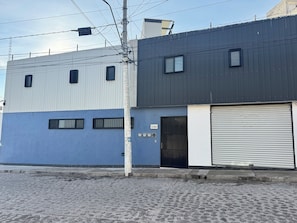 A building with a blue and grey facade, a closed metal shutter door, and a utility pole with wires. - Casa esperanza (Queretaro)